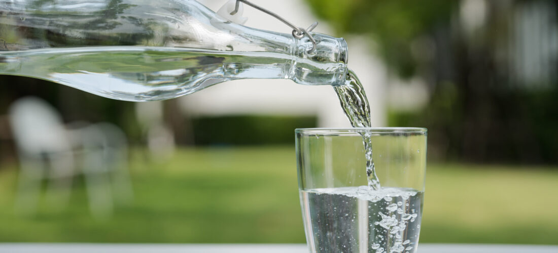 Pour the water from the water bottle into the glass in the garden around the house.